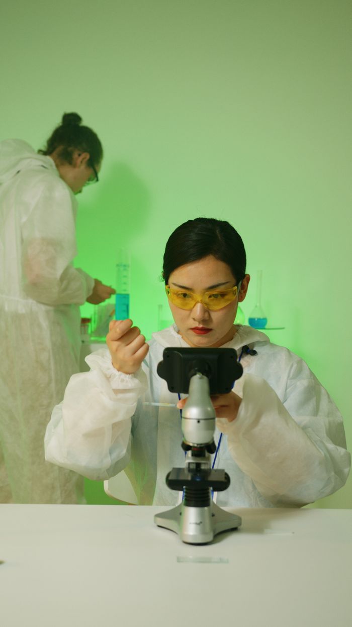 Two scientists in protective gear working in a laboratory setting with microscopes and test tubes.