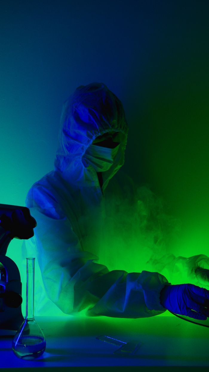 A scientist in protective gear works with green lighting in a laboratory setting.